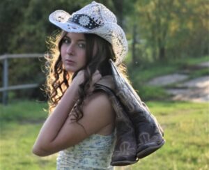 McKenna Faith Winters wearing a cowgirl hat and has cowboy boots over her shoulder
